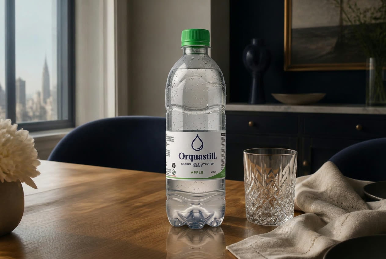 An Orquastill bottle and cut-crystal tumbler on an oak dining table in morning light